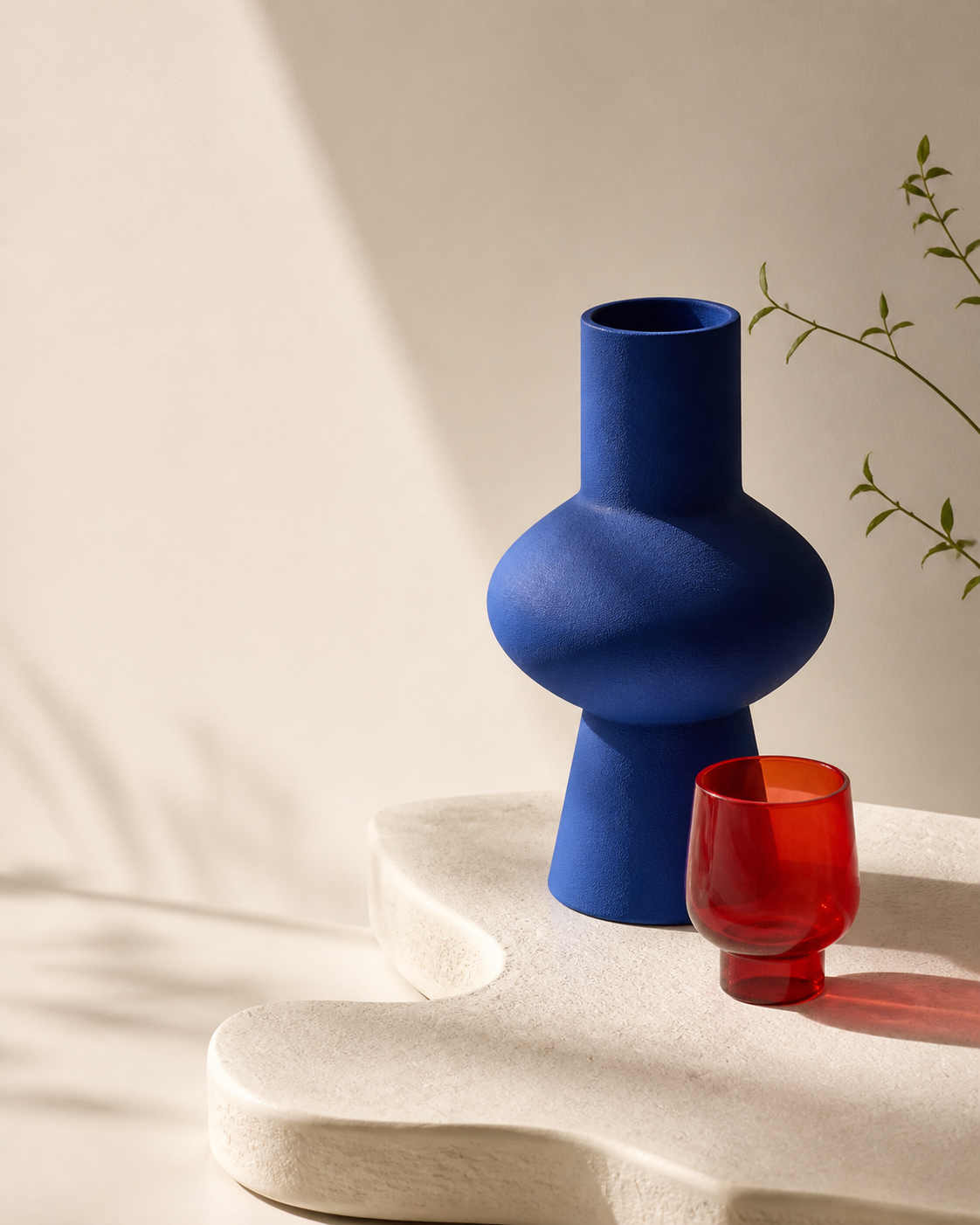 A blue ceramic vessel and red glass on a sculptural studio surface